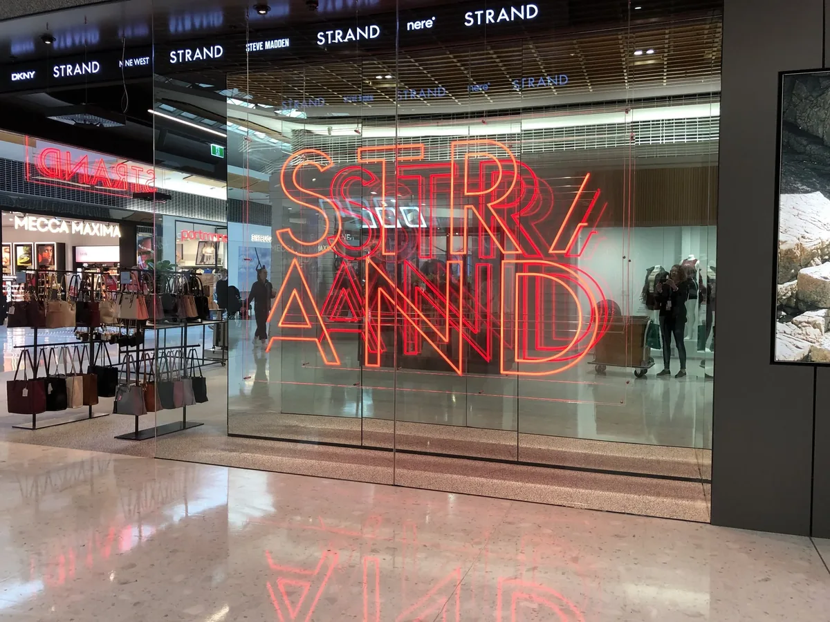 Frameless glass retail shopfront with illuminated signage behind the glazing
