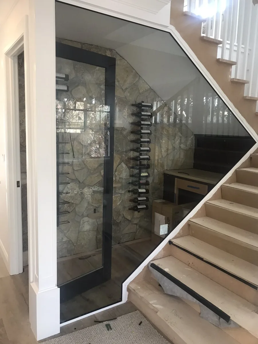 Angular frameless glass enclosure built beneath a stone-walled staircase