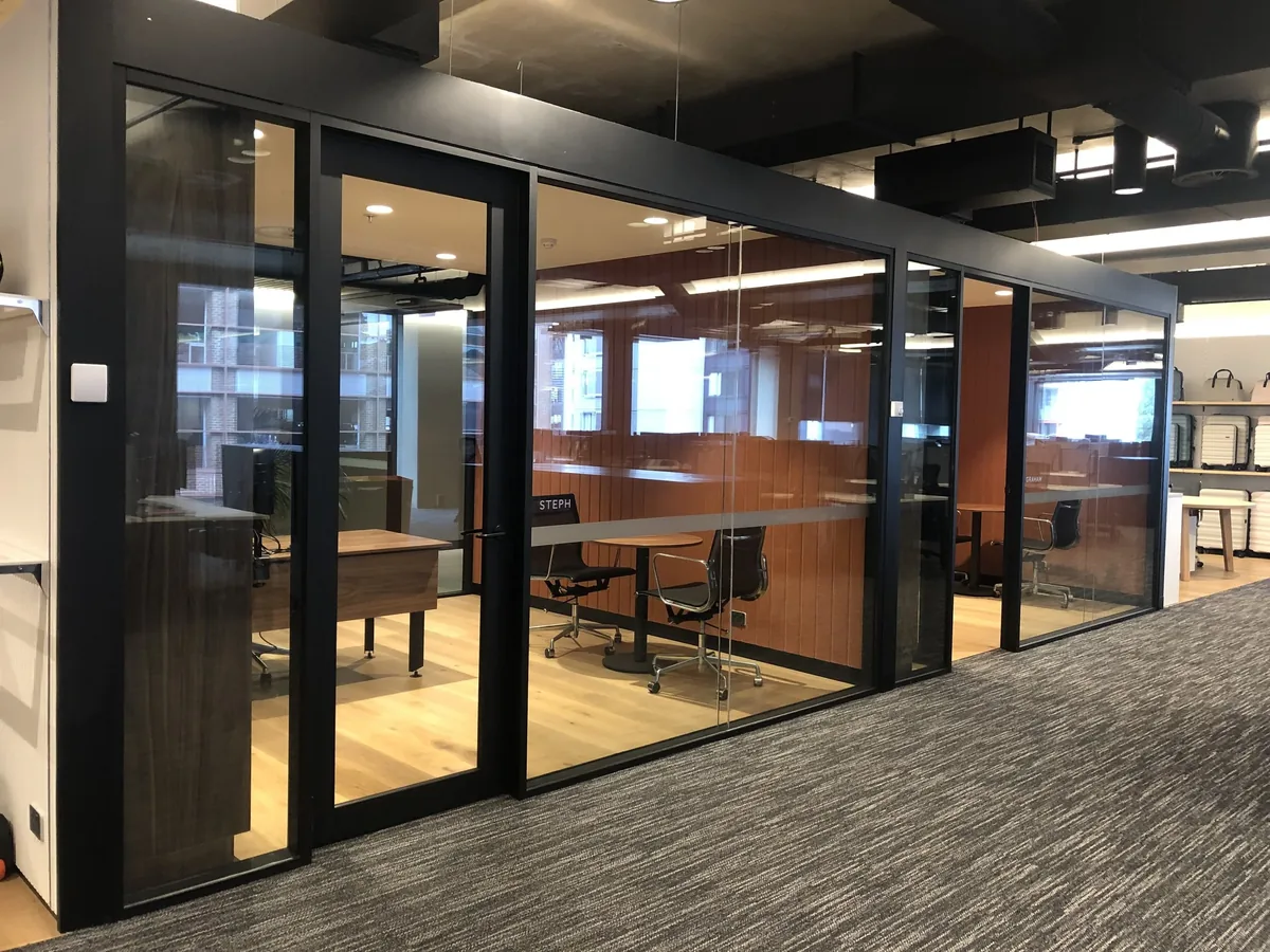 Aluminium-framed glass office rooms lining an open-plan workplace