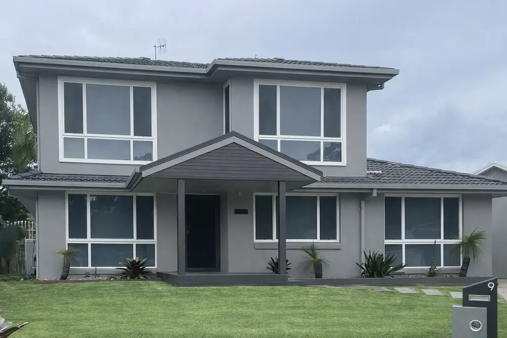 Dark security screen door at the covered front entry of a rendered two-storey home with aluminium-framed windows